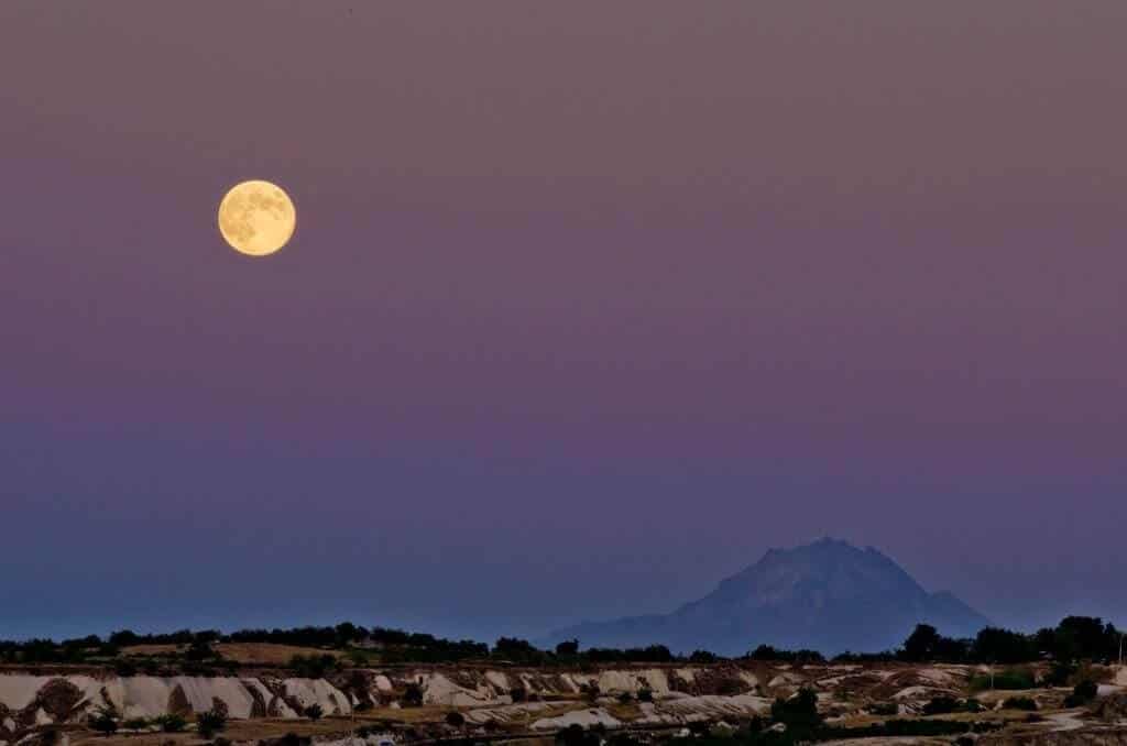 After sunset, moon on the upper left, a little hill on the  bottom right. Photograph.